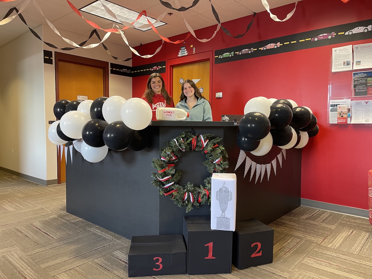 Person in front of desk with black and white balloons, streamers, and race podium