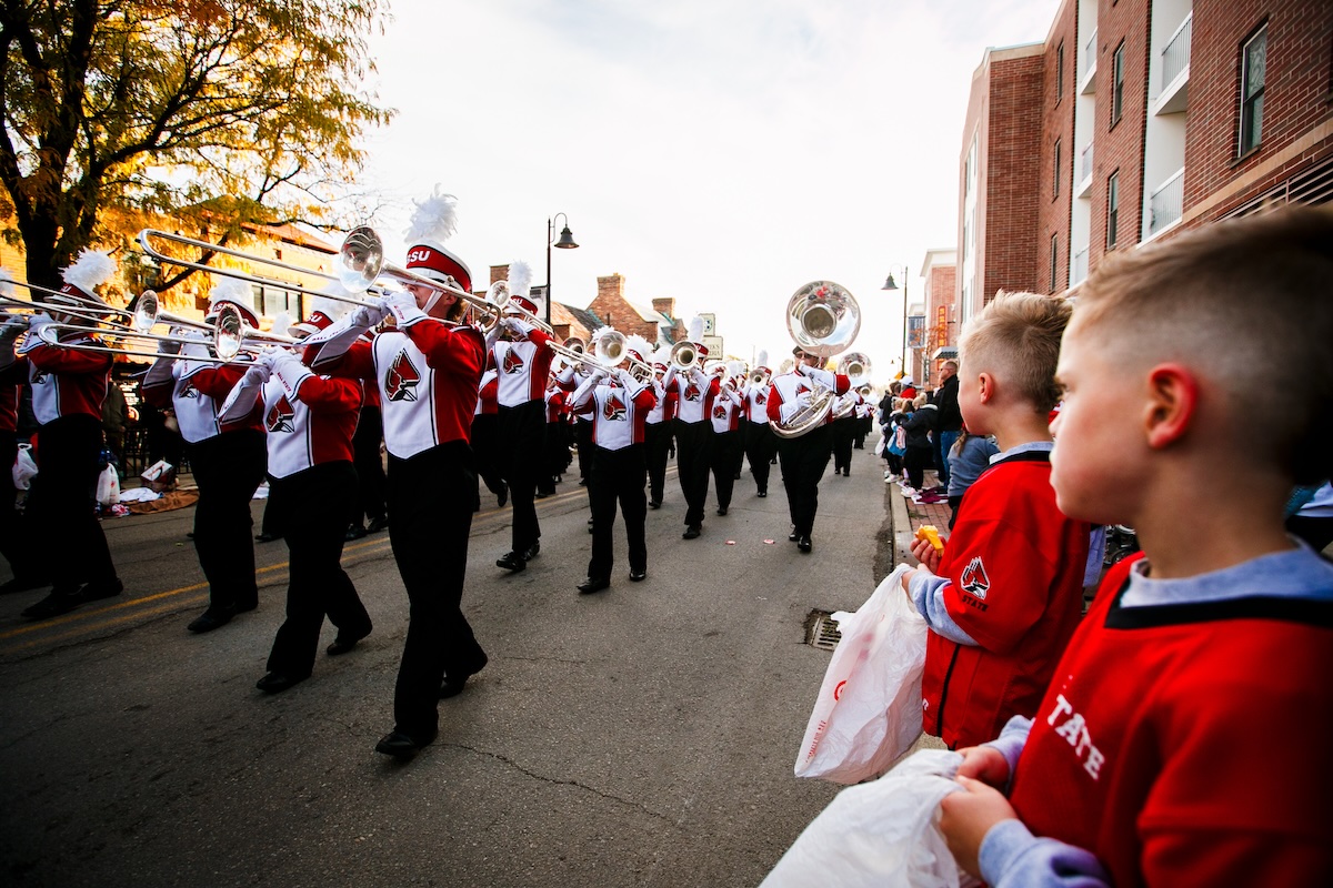 Band Marching in Village, with kids off to the side with bags of candy.