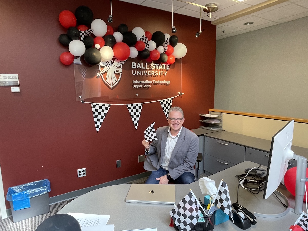 person sitting at desk with balloons and checkard flags in background