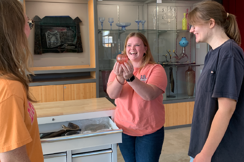 A workshop student shows off their glass pumpkin.