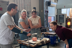 A group of people work on making a glass pumpkin at a glass blowing workshop.