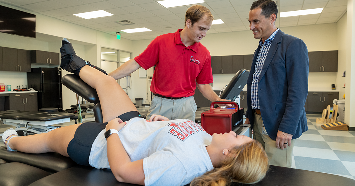 A male Ball State University student practicing athletic training on a female student while a male professor watches 