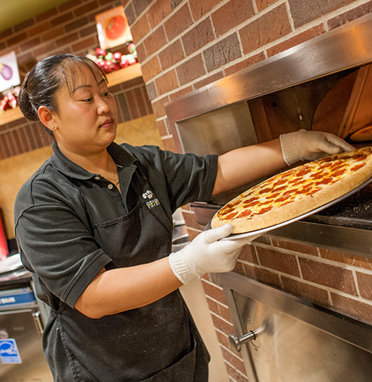 A Dining Service worker prepares a pizza