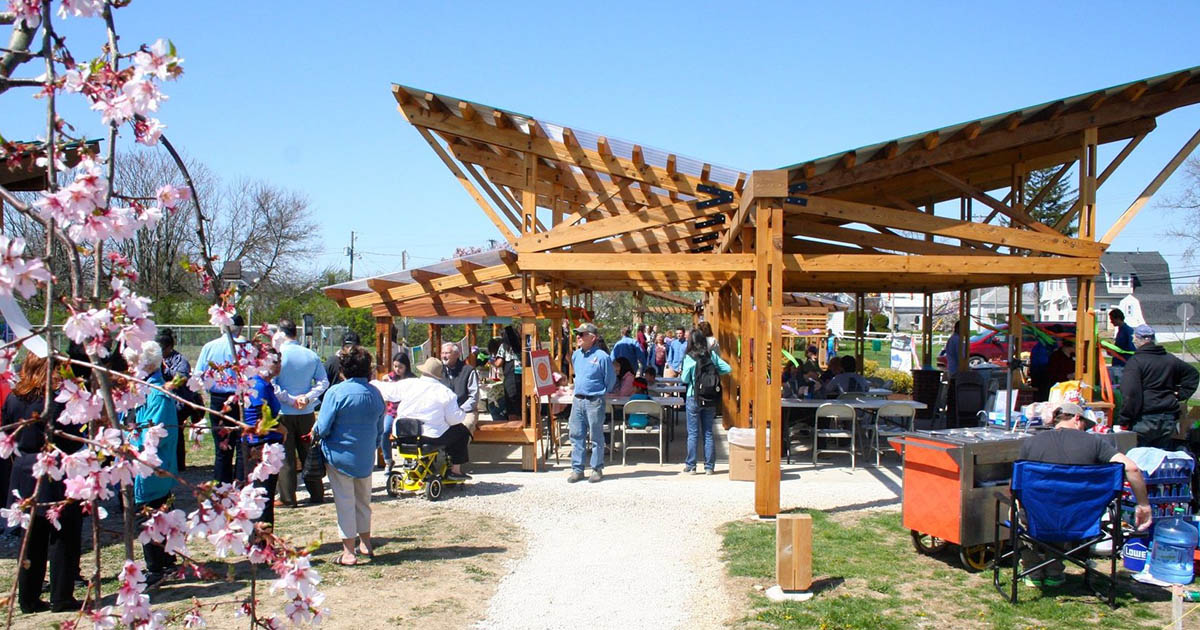 An organically-shaped pergola stands over a lively pavilion filled with people on a sunny day