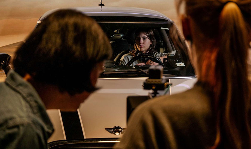 Person in a car in the background while other students film with a camera pointed at the car