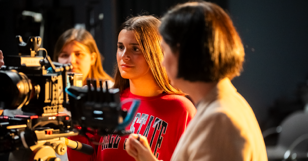 Students and a faculty member collaborate on a film production set while operating professional camera equipment.