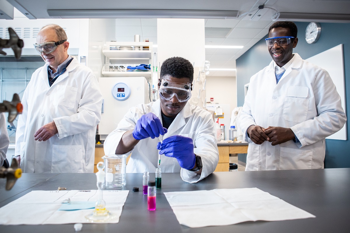 Student working with chemical wearing gloves with professor and another student behind