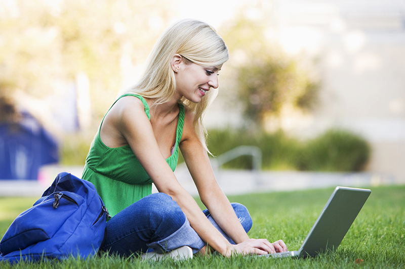 Student on computer while sitting on campus lawn