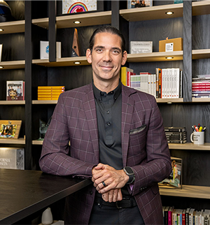 Marcus Hall poses in a purple plaid blazer in front of bookshelves in an office setting.