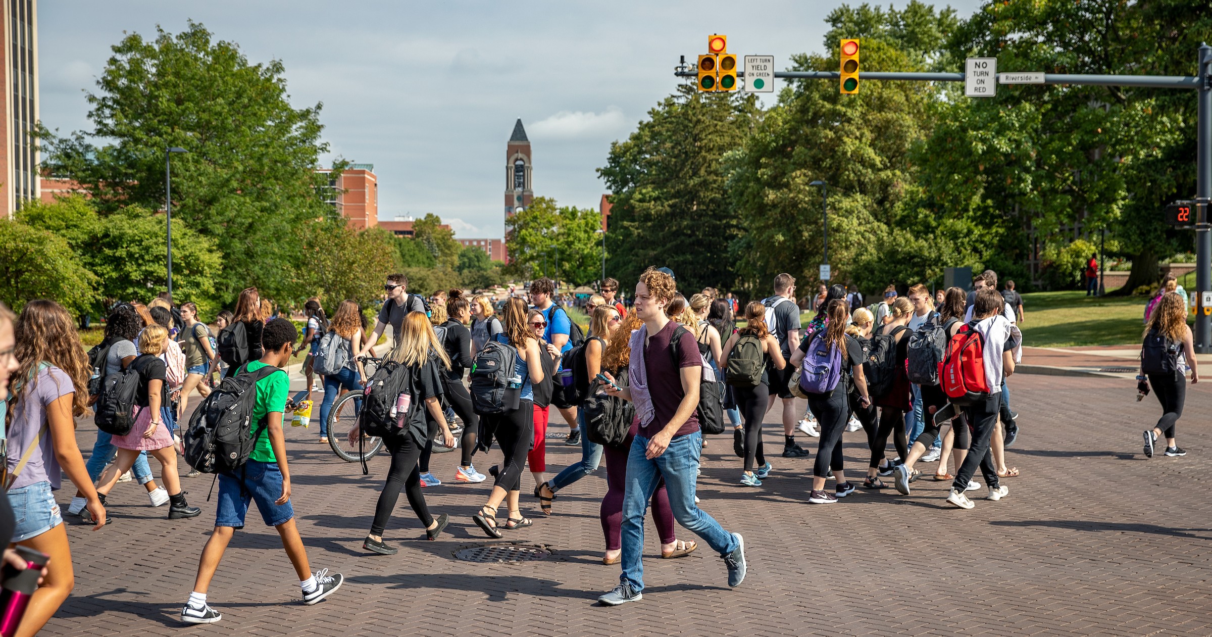 Group of 20 plus students crossing the street in front of the teachers college building at the scramble light on campus