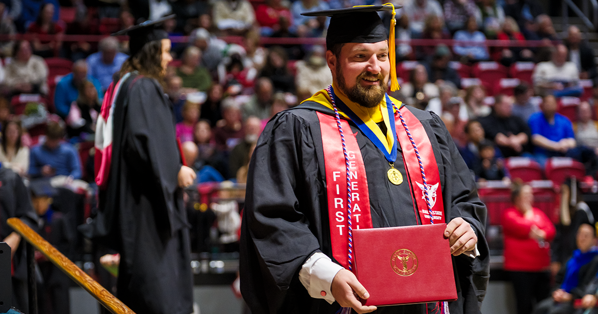 Male Ball State University student walking with a diploma at a graduation ceremony 