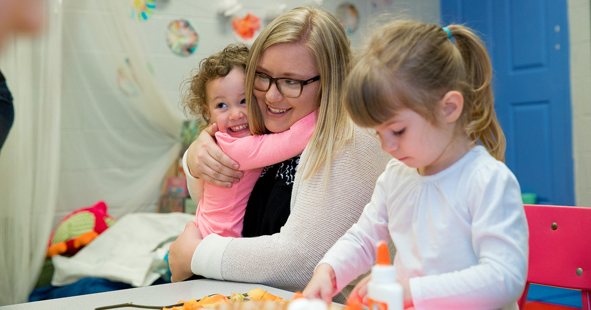 Children playing and hugging teacher.