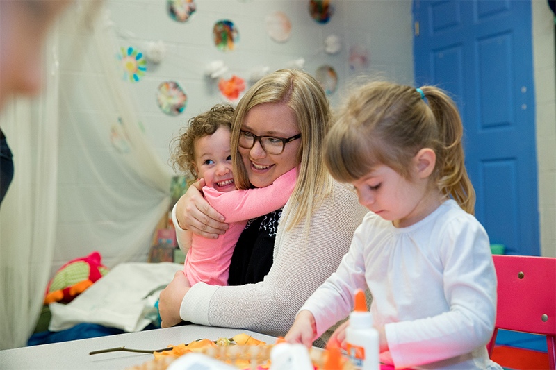 Children playing and hugging teacher.