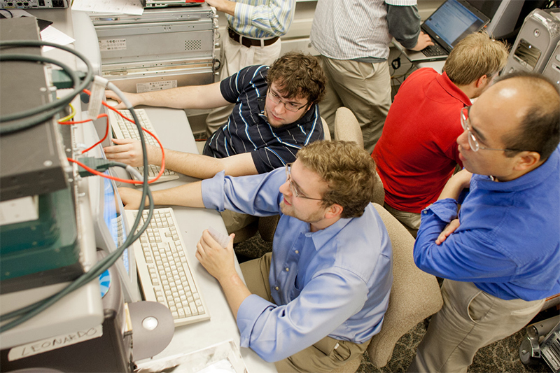 Students working on computers while teacher watches.