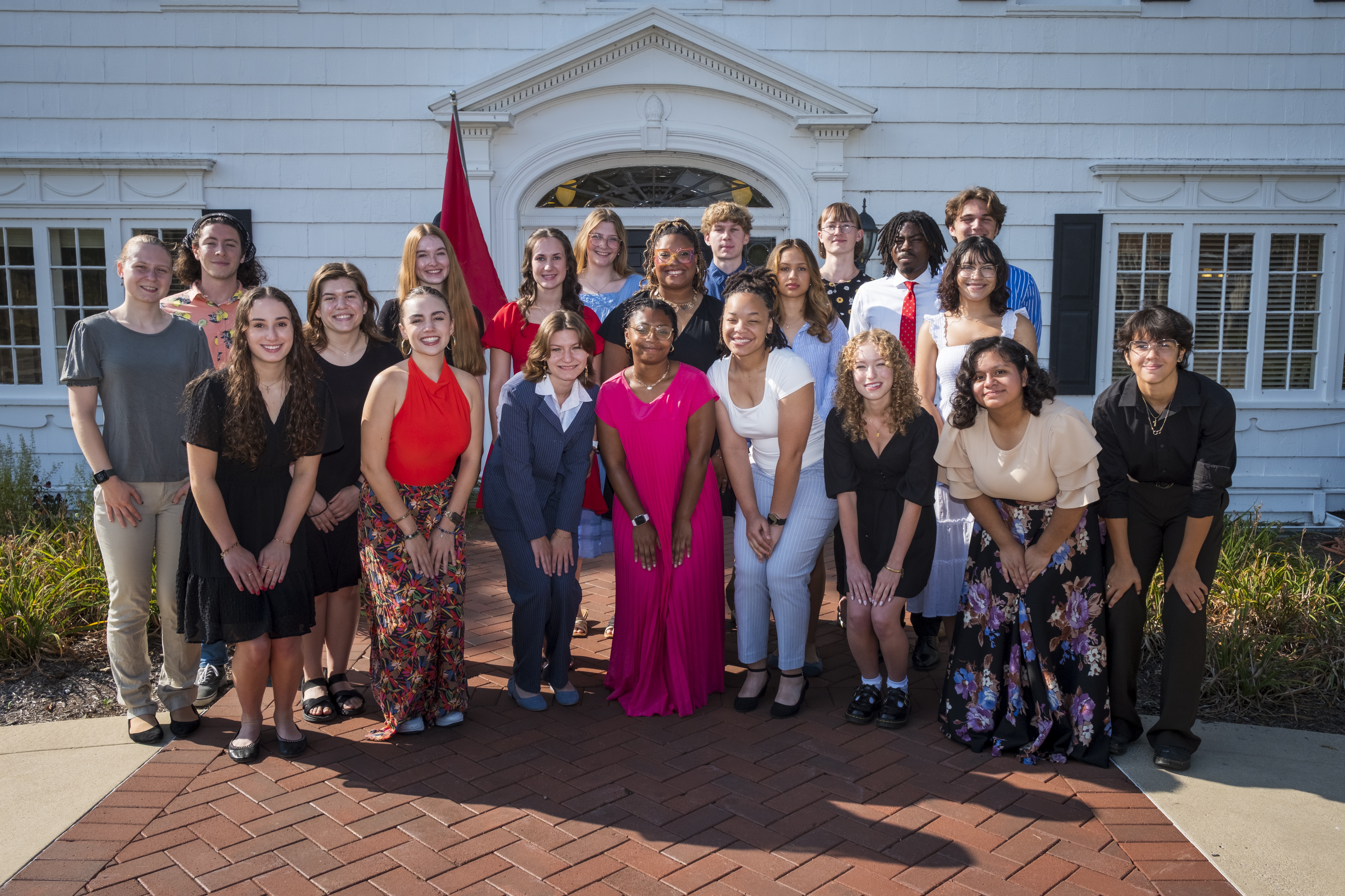 Group photo of Ball State University students posing in front of a white building with a red flag 