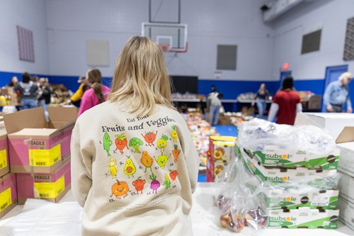 A student sorts items at a food drive wearing a ahirt that says Eat your fruits and veggies.