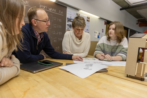 A group of students and faculty look at architecture plans