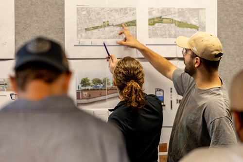 Students point up at landscape plans on a wall