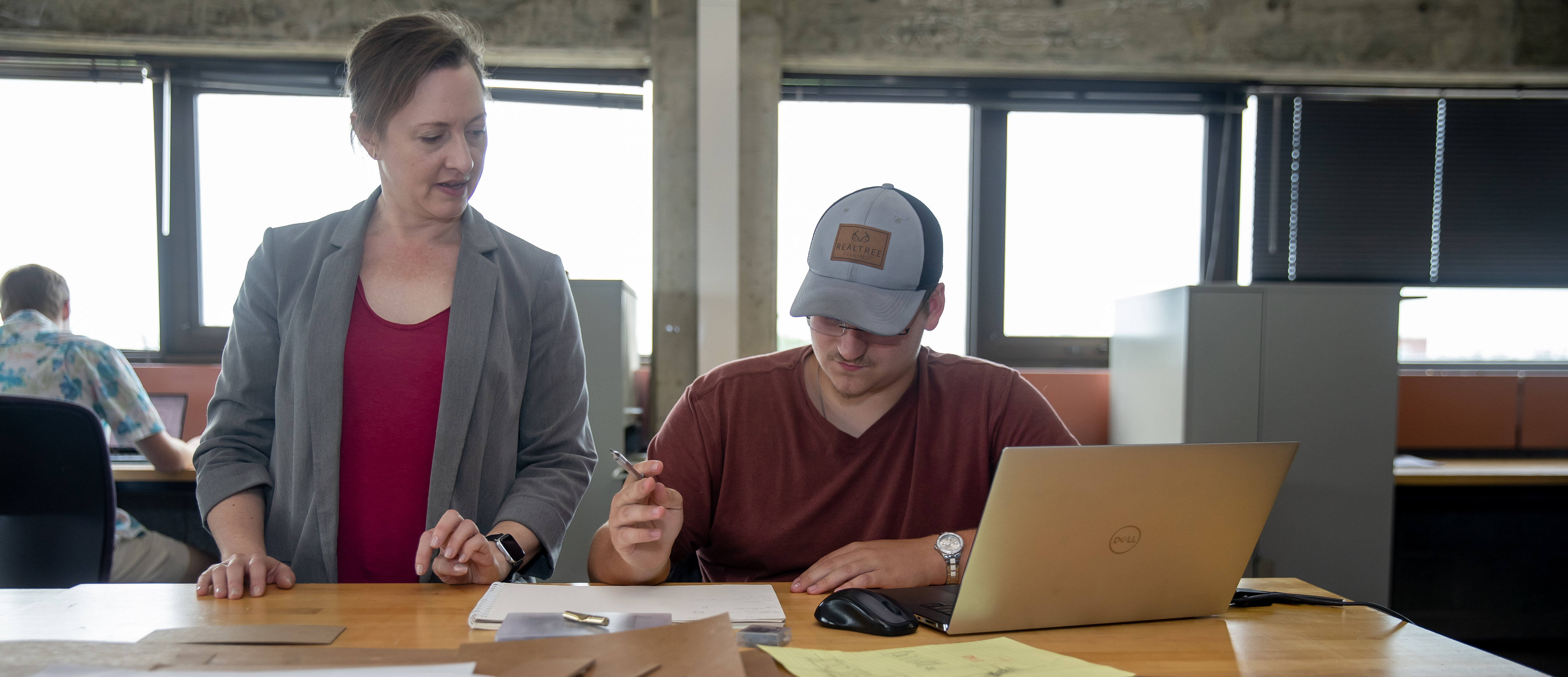 A professor and students stand together over a drafting table. 
