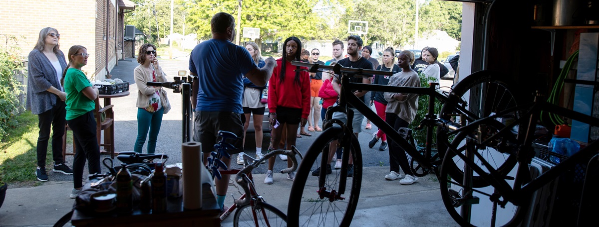 A group of speakers listen to a speaker with bikes in the foreground.