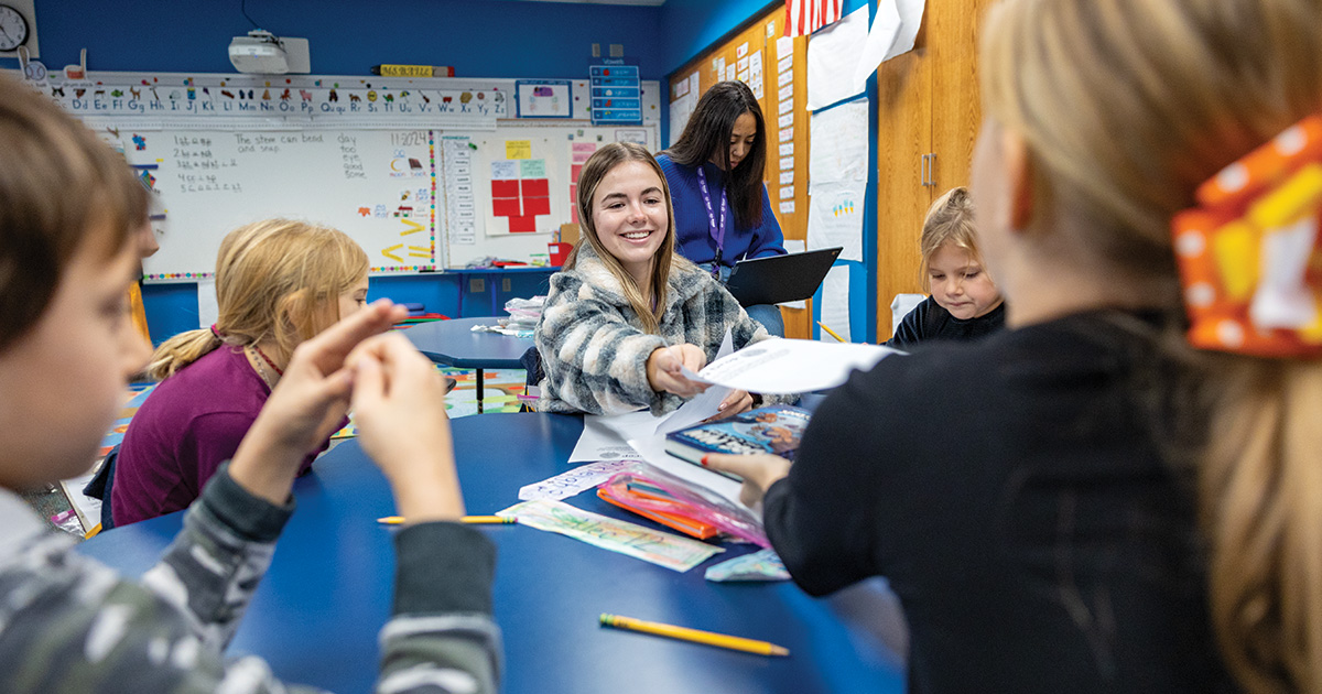 Elementary age students around a table one is smiling handing a paper to another