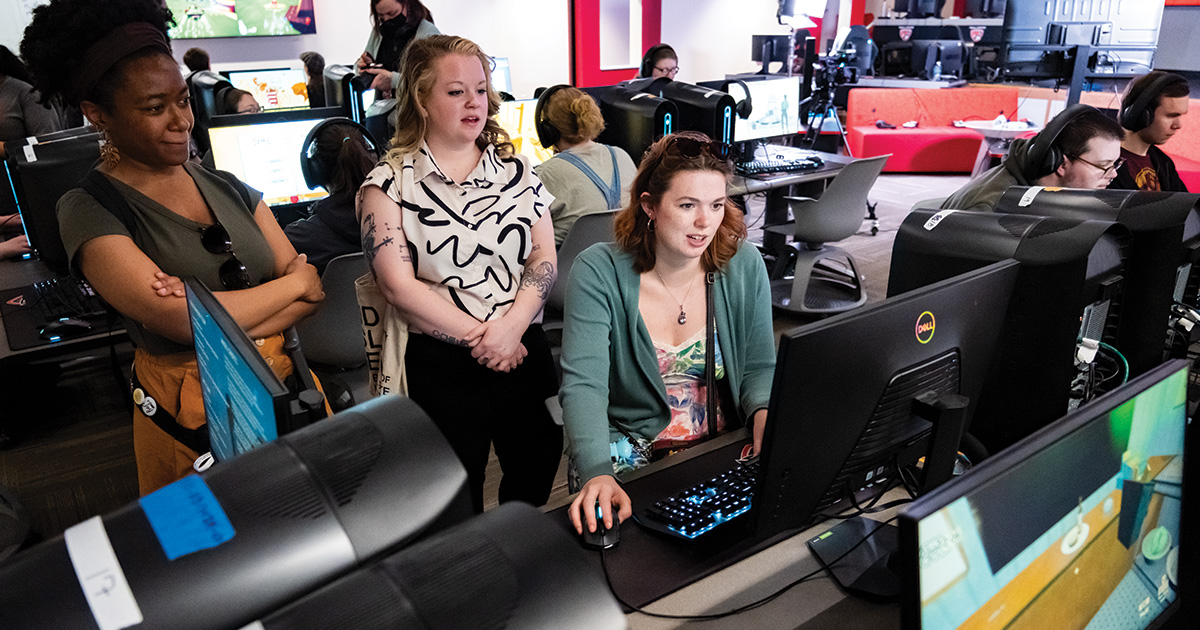 Student at computer playing game with two other students watching