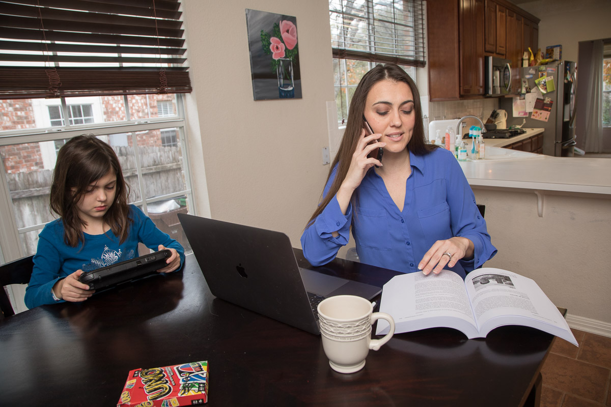 Malena Price seated in front of a laptop with phone, book, and child next to her
