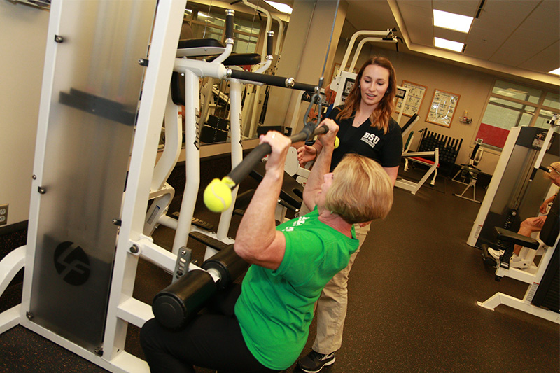 A woman lifts weights as a student looks on.