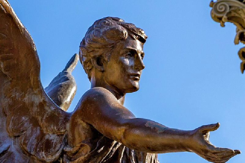 Close up view of the Beneficence statue in front of a blue sky. 