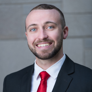 Jason Fry, smiling and wearing a black suit with a red tie and white undershirt