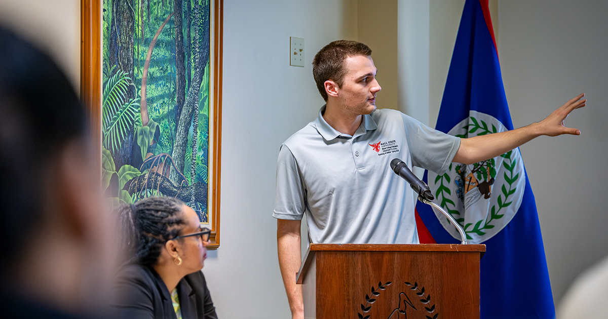 Student presents information at a podium during an international learning experience, with attendees listening in a conference room.