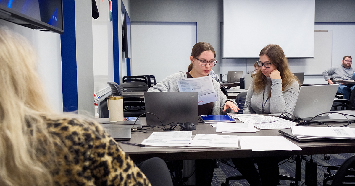 Accounting students review tax documents and work together at laptops during a Volunteer Income Tax Assistance (VITA) program session.