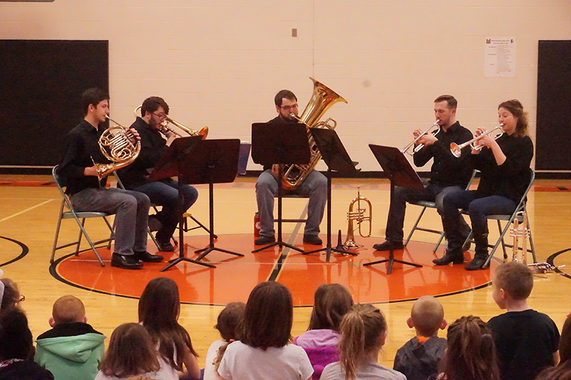Students performing as a brass quintet on a gymnasium floor