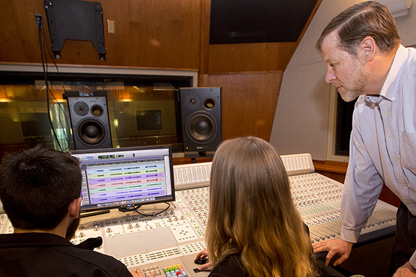 instructor and two students working on music media production in a studio