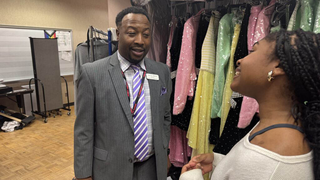 Male principal talking with a female student in front of choir costumes.