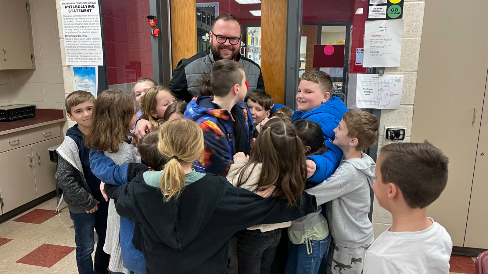 Students hugging in a classroom while Chad Crews looks at them with a smile