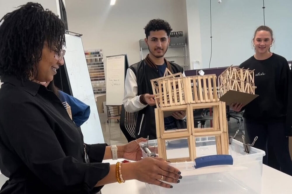 Two interior design students and one instructor looking at a construction model made of wood