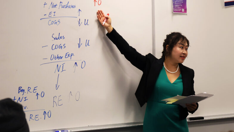 Online Master’s in Accounting faculty Sharon Huang in a classroom gesturing toward a whiteboard