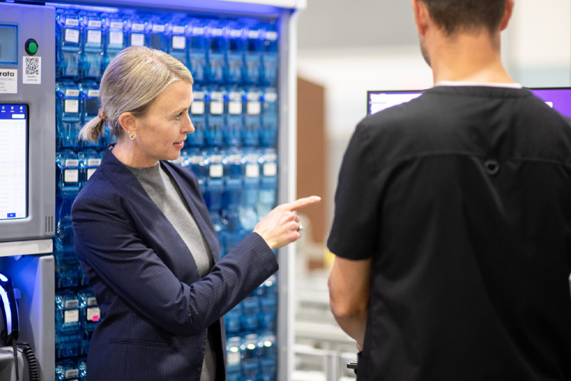 Leslie Hurst in a blue blazer to the left pointing with her index finger at a screen. Male with his back turned looking at the screen that Leslie is pointing to