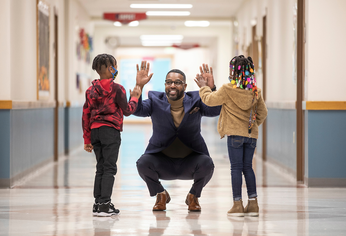 A school administrator high-fives two young students in a school hallway