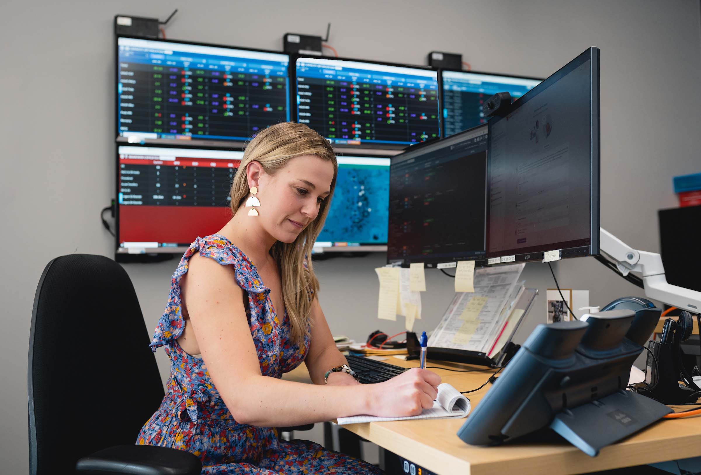 Female student sitting at the computer with three monitors at the desk and several monitors in the background on the wall