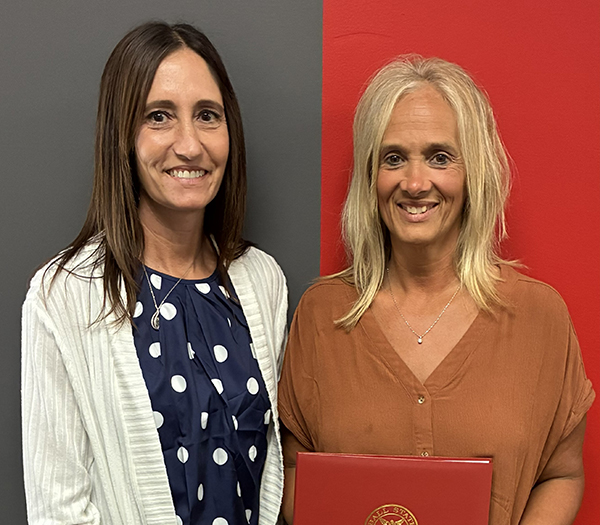 Two Ball State University employees pose for a recognition photo, one holding a red Ball State presentation folder.