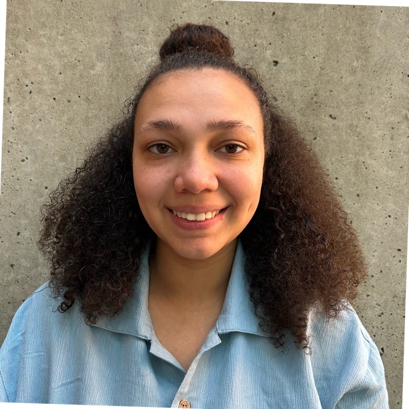 Alyson Quirk smiling while wearing a light blue collared shirt, posing in front of a concrete wall.