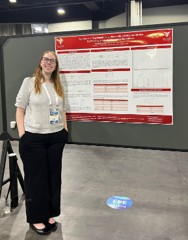 Anastasia Faddis stands beside her research poster at an academic conference.