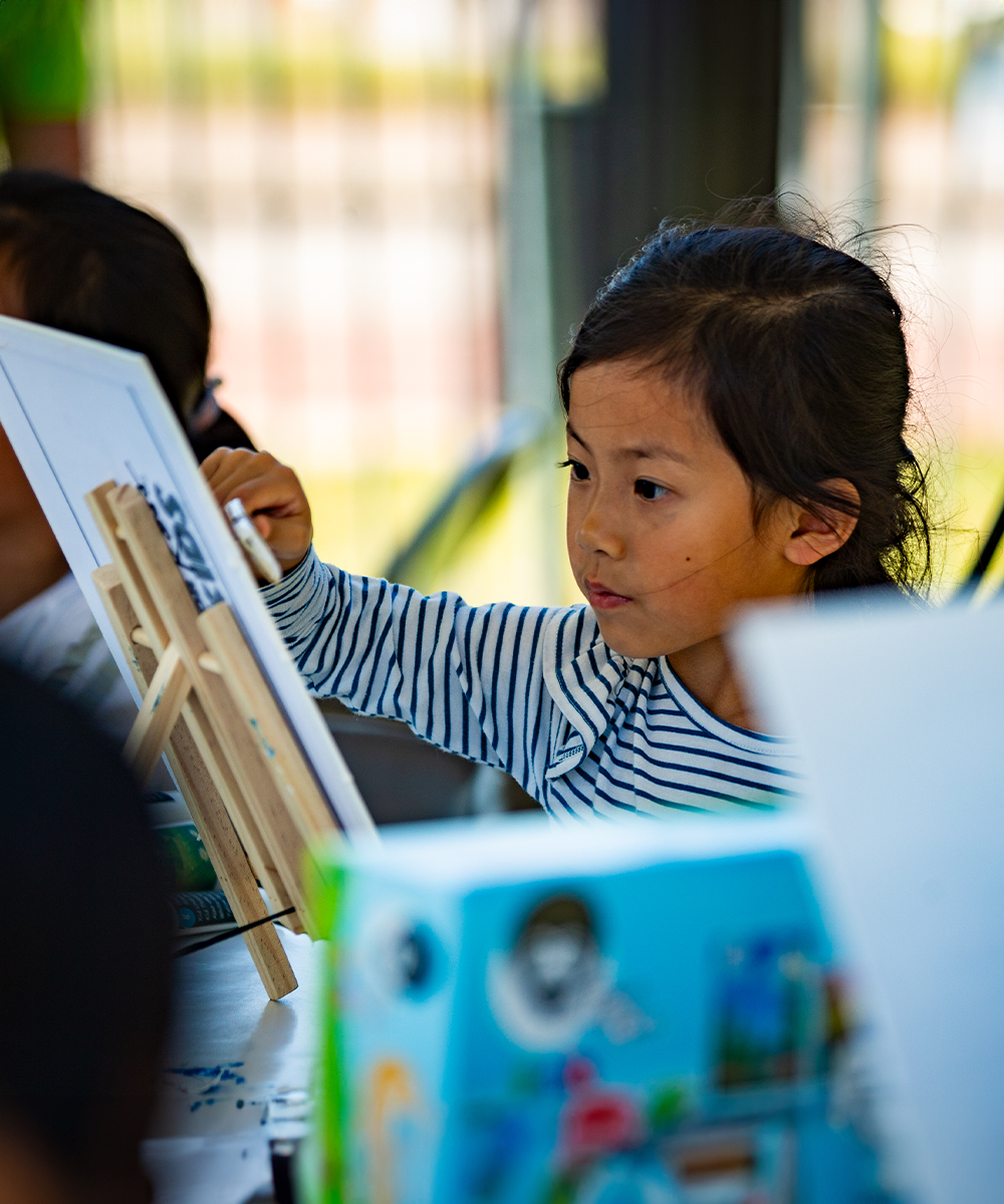 A young girl painting at a Ball State art event.
