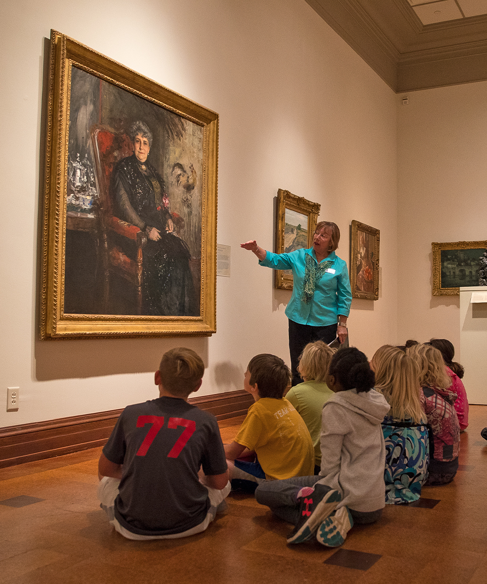 Elementary-aged students sitting on the floor as an instructor shows them a painting at Ball State's David Owsley Museum of Art.