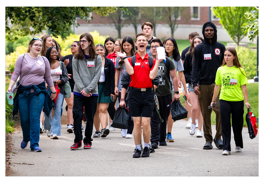 Orientation students walking in a group of 20-25 students with name tags on. Orientation leader in the front with red polo 