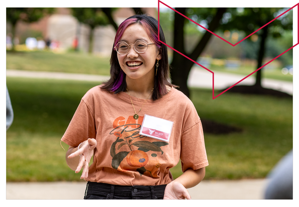 Female student with dark hair and glasses at orientation outside with green space behind her