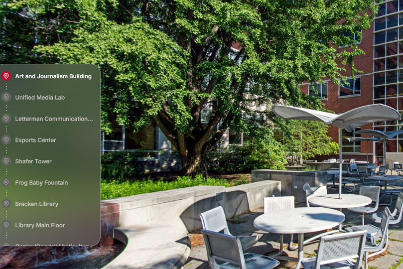 Campus Reel screenshot with list of buildings on the left and Arts and Journalism terrace on the right-silver table and chairs outside on patio with umbrella, tree in the background outside of a building