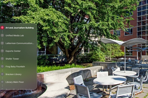 Campus Reel screenshot with list of buildings on the left and Arts and Journalism terrace on the right-silver table and chairs outside on patio with umbrella, tree in the background outside of a building